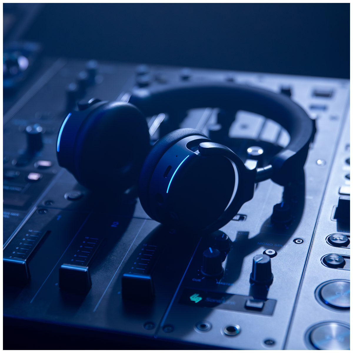 AlphaTheta HDJ-F9 Professional Wireless DJ Headphones resting on a DJ mixer console, lit with dramatic blue and black ambient lighting.