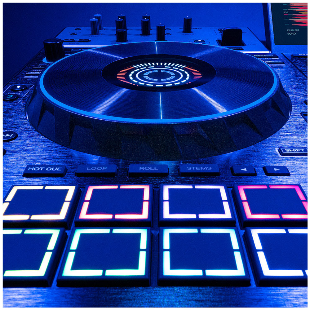 A close-up of a DJ controller with a large illuminated vinyl record-shaped platter and multiple square touch pads lit in blue, pink, and white under dramatic blue lighting.