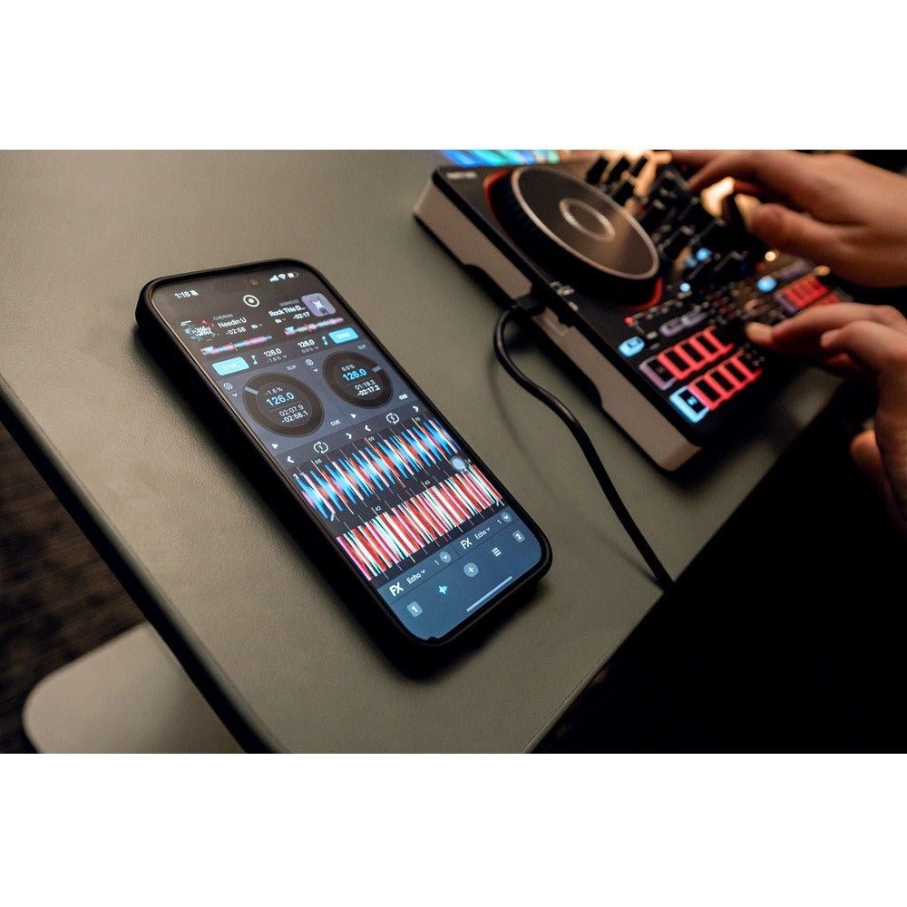 A smartphone displaying a DJ software interface connected to a DJ controller, with a person's hands operating the controller on a dark table.