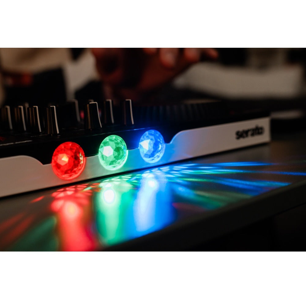 A close-up of a Serato DJ controller showing three illuminated crystal-like buttons in red, green, and blue, with the brand name 'serato' visible on the side and colorful light reflections on the surface below.